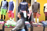 Mannequins exibem roupas e preços em loja. Caixas de vestuário e pessoa desfocada em primeiro plano.