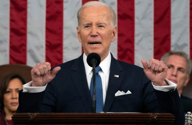 Joe Biden discursa em pódio, gesticulando com as mãos à frente de uma bandeira dos EUA.