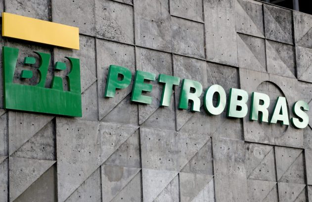 Logotipo verde "BR" com barra amarela e letras verdes "PETROBRAS" em fachada de concreto texturizado.