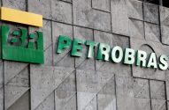 Placa da Petrobras: logo "BR" verde e amarelo, e nome "PETROBRAS" verde, em parede de concreto texturizado.