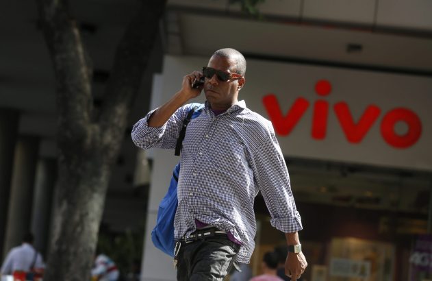 Homem de camisa xadrez caminhando e falando ao celular, com logo "Vivo" ao fundo.