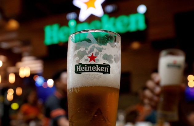 Copo de cerveja Heineken com espuma. Fundo desfocado com letreiro neon da marca e estrela em um bar.