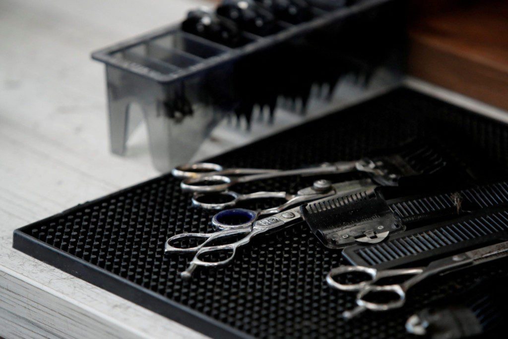 Ferramentas de barbeiro: tesouras e pentes sobre um tapete preto.