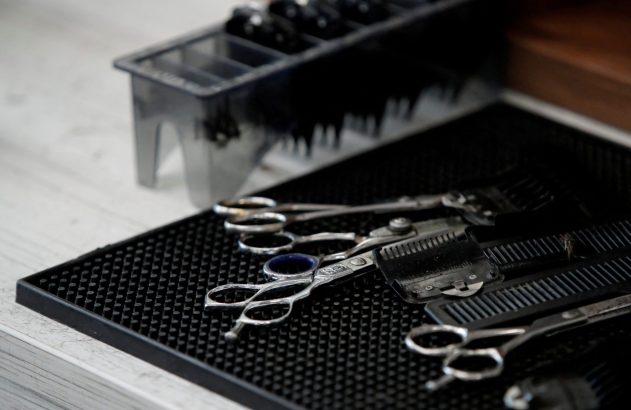 Ferramentas de barbeiro: tesouras e pentes sobre um tapete preto.