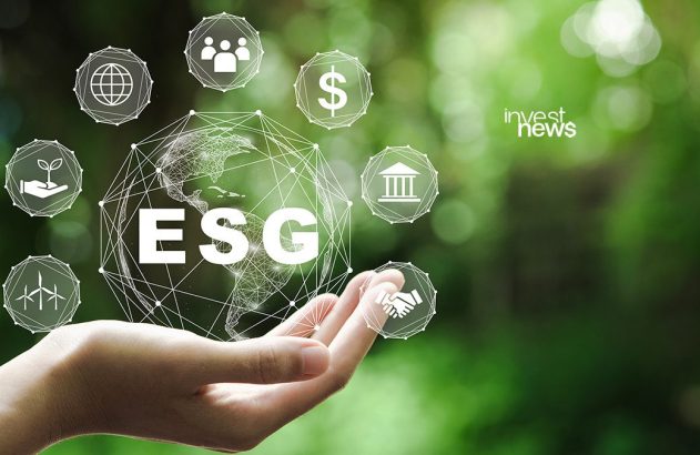 Mão segura globo digital com "ESG" e ícones de ambiente, social e governança. Fundo verde desfocado.