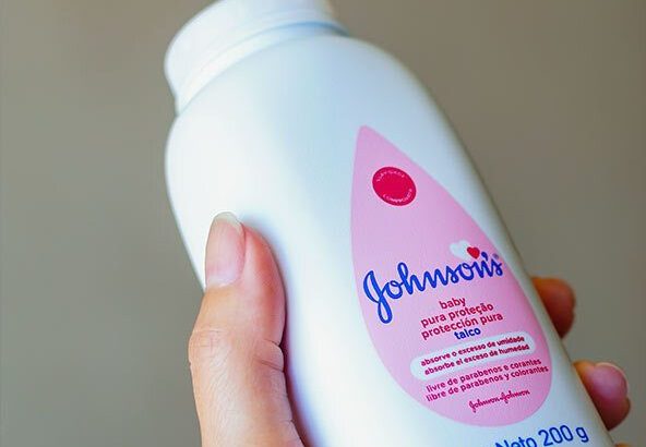 Mão segurando um frasco de talco Johnson's Baby com rótulo rosa.