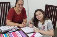 Mulher e menina sorrindo estudam juntas à mesa.