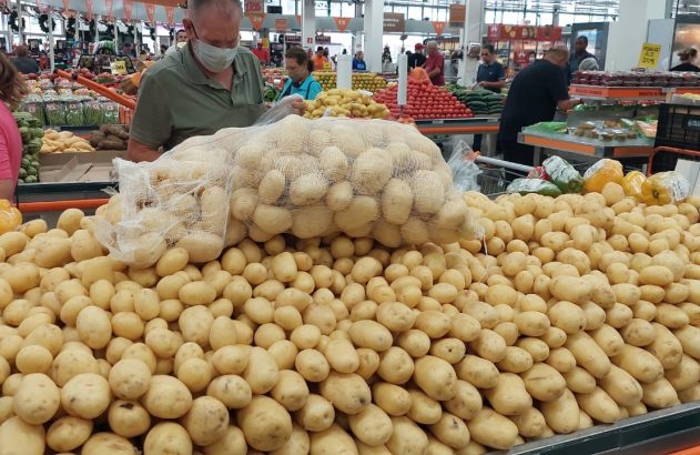 Grande pilha de batatas frescas e outros vegetais. Clientes em um supermercado fazendo compras.