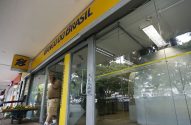 Pessoas em frente ao Banco do Brasil; um fala no celular, outro perto de carrinho de frutas.