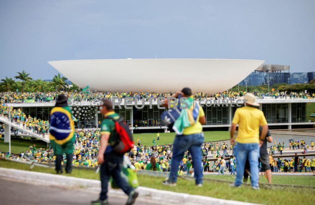Multidão com roupas verde-amarelas em frente ao Congresso Nacional em Brasília, sob céu parcialmente nublado.