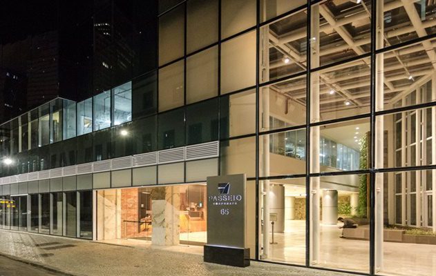 Edifício corporativo moderno de vidro com fachada iluminada à noite e letreiro "Passeio Corporate 65".