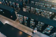 Vista aérea: pessoa lendo em biblioteca com longas estantes cheias de livros.