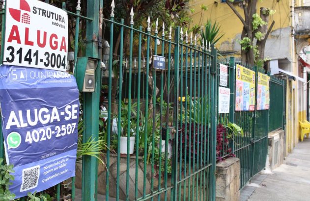 Grade verde com placas de 'Aluga-se' e 'Proibido Estacionar' em calçada urbana.