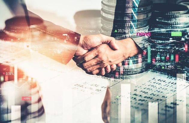 Aperto de mãos sobre fundo de gráficos financeiros, pilhas de moedas e skyline da cidade.