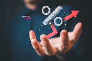 Mão exibe símbolo de % e gráfico de seta vermelha em ascensão. Indica aumento percentual ou crescimento.