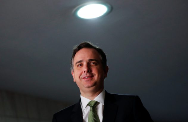 Homem de terno sorrindo e olhando para cima, sob uma luz brilhante no teto escuro.