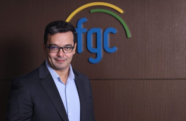 Homem de óculos, paletó, sorrindo. Fundo com logo 'FGC' azul e arcos coloridos.