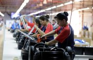 Mulheres uniformizadas montam carrinhos elétricos em linha de produção.