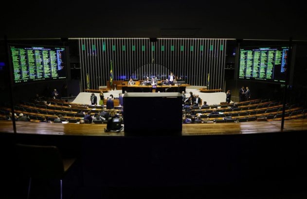 Plenário do Congresso, com parlamentares em assentos curvos e painéis digitais exibindo informações da sessão.