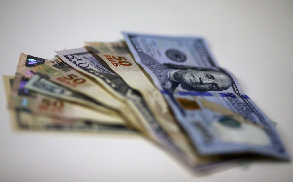 Leque de várias notas de dólar, de diferentes valores, sobre fundo claro.