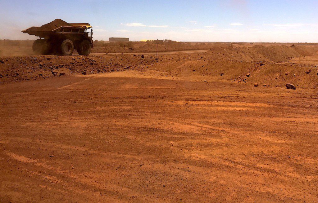 Caminhão de mineração com carga em estrada de terra. Cenário de mina a céu aberto sob céu azul.