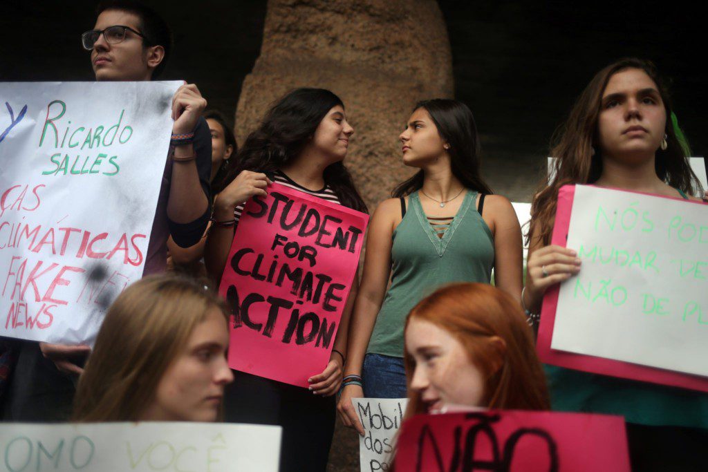 Jovens protestam com cartazes, um rosa diz "STUDENT FOR CLIMATE ACTION".