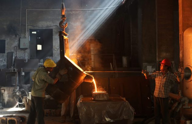 Dois trabalhadores despejam metal incandescente em uma fundição, com raios de sol e faíscas.