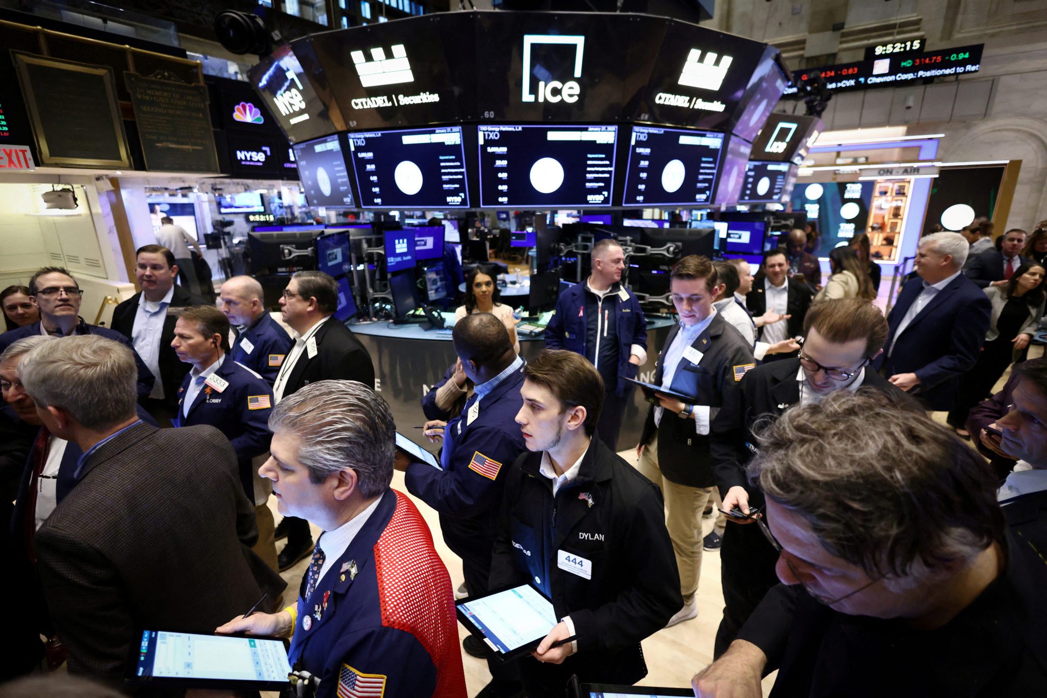 Movimentado pregão da NYSE com corretores e telas exibindo cotações financeiras em tempo real.