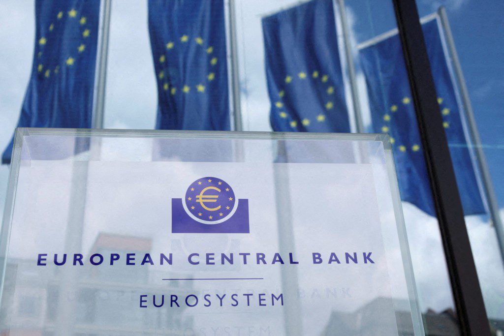Placa do Banco Central Europeu com logo do euro e bandeiras da União Europeia ao fundo.