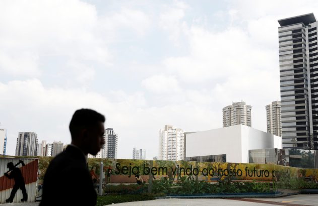 Silhueta de pessoa caminha em frente a prédios altos e muro com "Seja bem vindo ao nosso futuro".