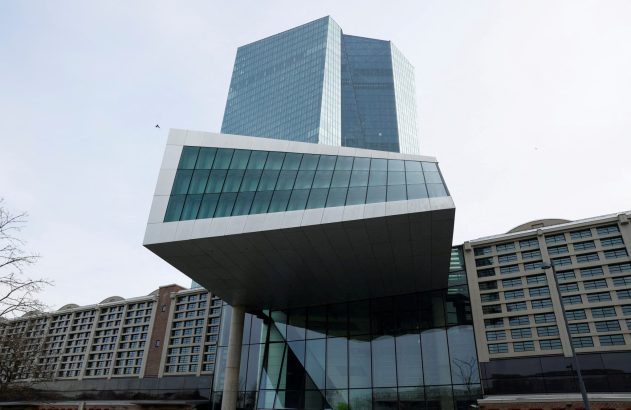 Edifício moderno de vidro e concreto com estrutura saliente, e arranha-céu ao fundo, sob céu nublado.