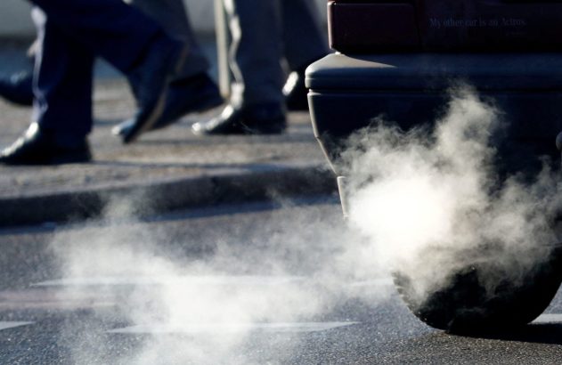 Fumaça espessa saindo do escapamento de um carro, com pedestres caminhando ao fundo.