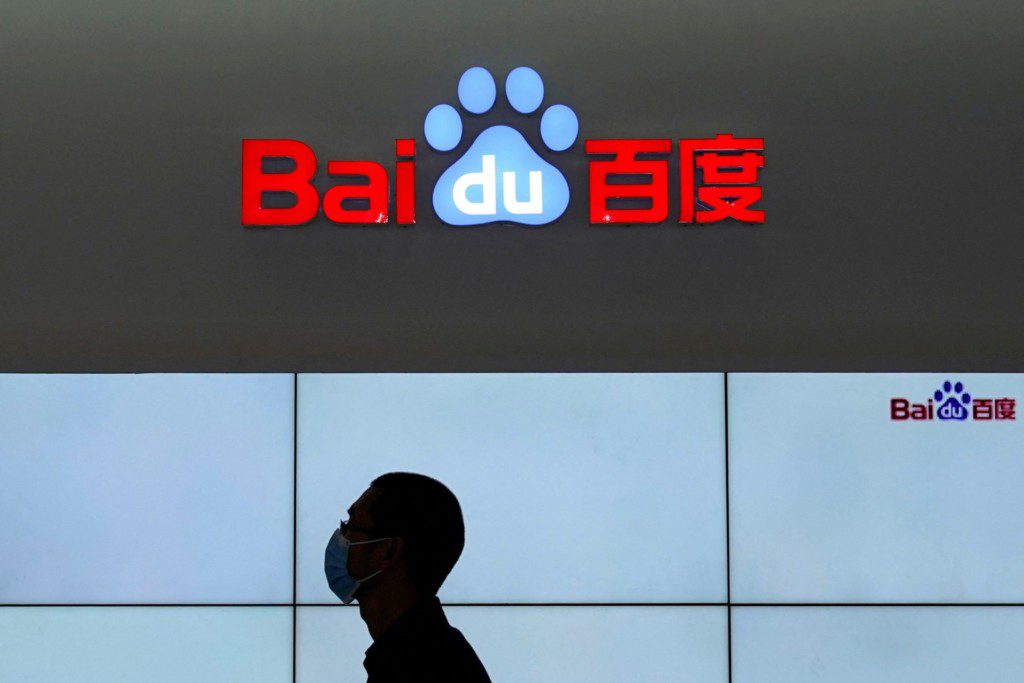 Logo Baidu iluminado com pessoa de máscara em silhueta contra telas brancas.