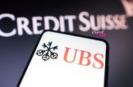 Logos UBS em smartphone e Credit Suisse em fundo, simbolizando a aquisição bancária.