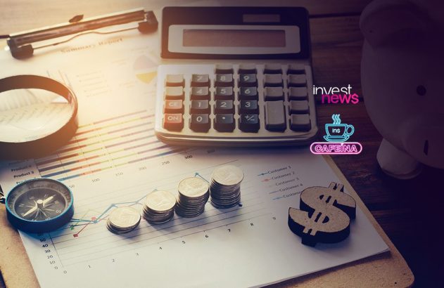 Mesa com documentos financeiros, calculadora, moedas, lupa e cofrinho. Representa análise e investimento.