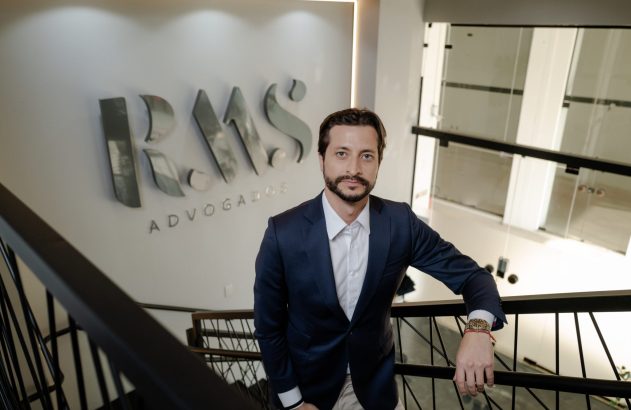 Homem de terno parado em escadaria de escritório com logo 'RMS ADVOGADOS' ao fundo.