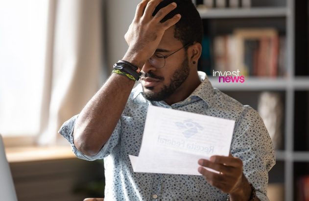 Homem segura documento da Receita Federal e põe a mão na testa, com expressão de preocupação.