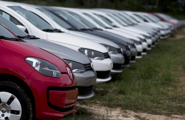Fila de carros de cores variadas estacionados em campo. O primeiro é vermelho.