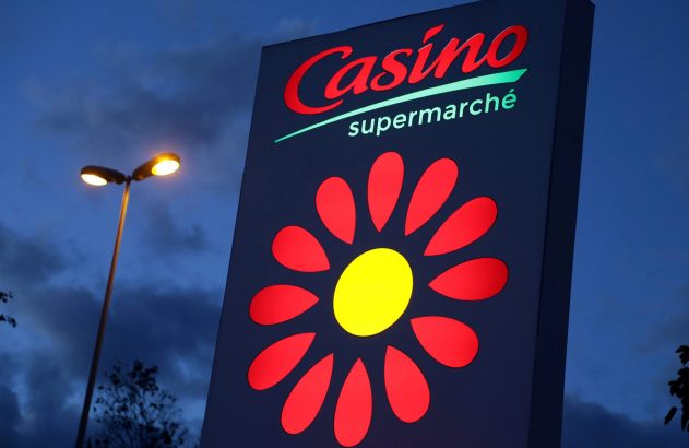 Um letreiro iluminado da Casino Supermarché com poste de luz, à noite.