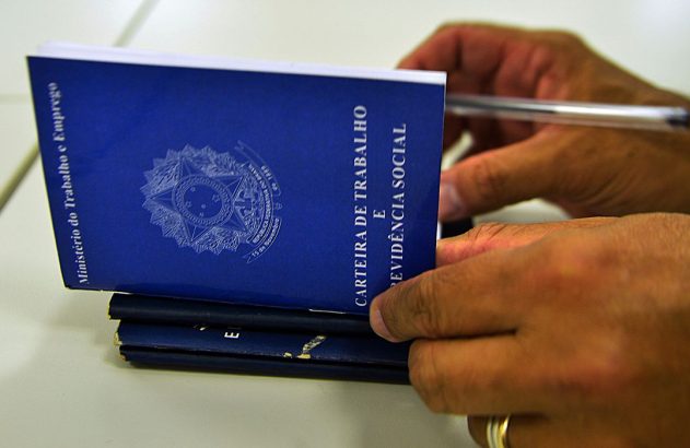 Mãos de um homem preparando Carteiras de Trabalho e Previdência Social, com uma caneta por perto.