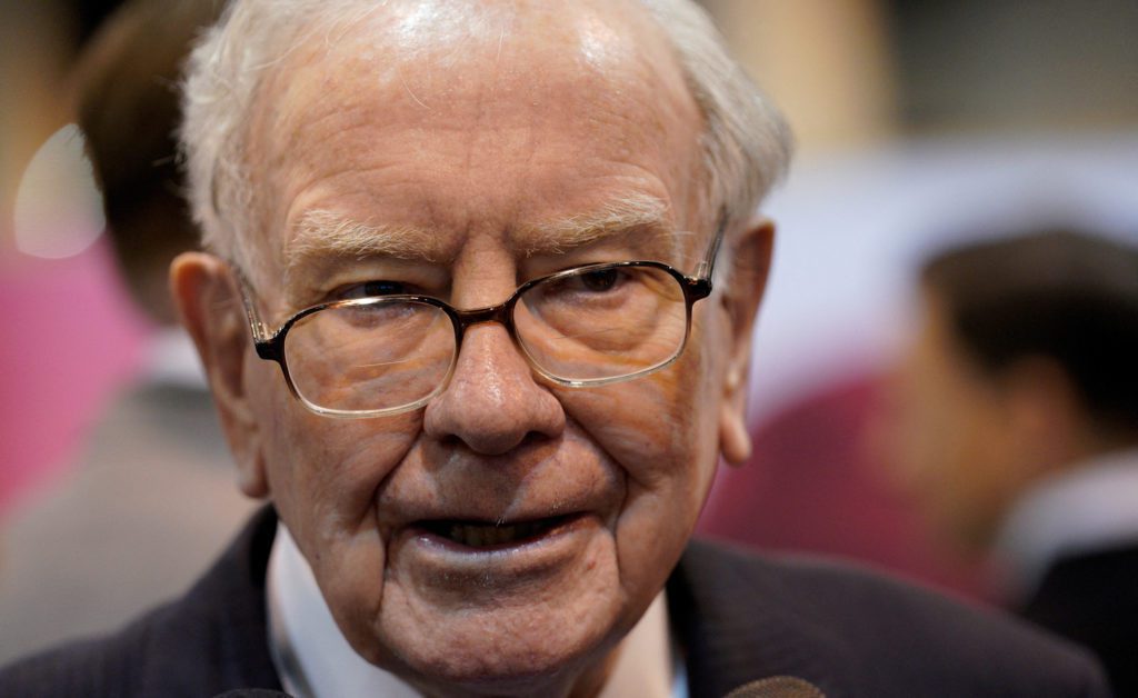 Rosto de Warren Buffett, idoso com óculos, olhando e sorrindo.