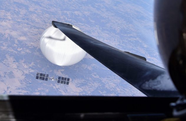Balão branco de alta altitude e objeto em forma de satélite, vistos da asa de um avião sobre a Terra.