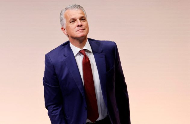 Homem de terno azul e gravata vermelha, olhando para cima e à direita com expressão séria.