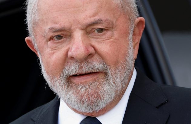 Close-up de homem com barba grisalha, terno e gravata, com boca entreaberta.
