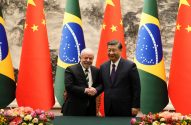 Presidentes Lula e Xi Jinping se cumprimentam entre bandeiras do Brasil e China.