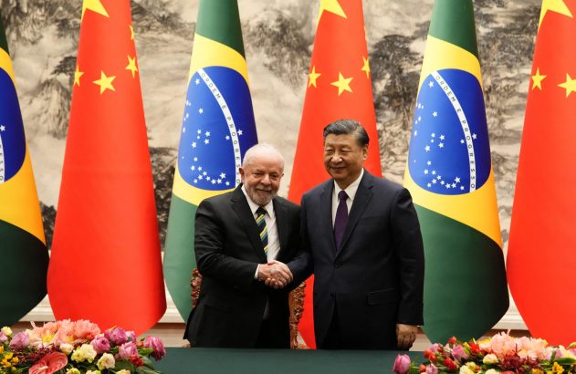Presidentes Lula e Xi Jinping se cumprimentam entre bandeiras do Brasil e China.