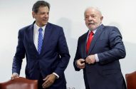 Fernando Haddad sorri ao lado de Lula, de terno escuro e gravata vermelha, ajeitando o paletó.