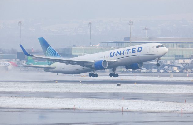 Avião da United Airlines decolando em aeroporto coberto de neve e céu nublado.