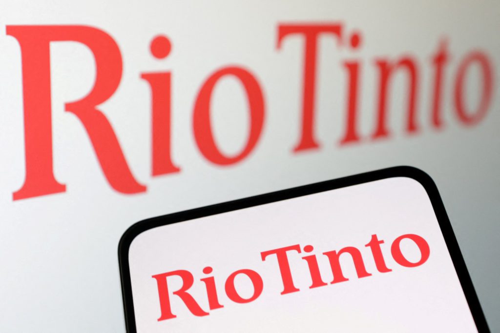 O nome "Rio Tinto" exibido em uma tela grande no fundo e em um smartphone no primeiro plano.