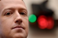 Mark Zuckerberg em close-up, olhando fixamente. Fundo desfocado com luzes verdes e vermelhas.